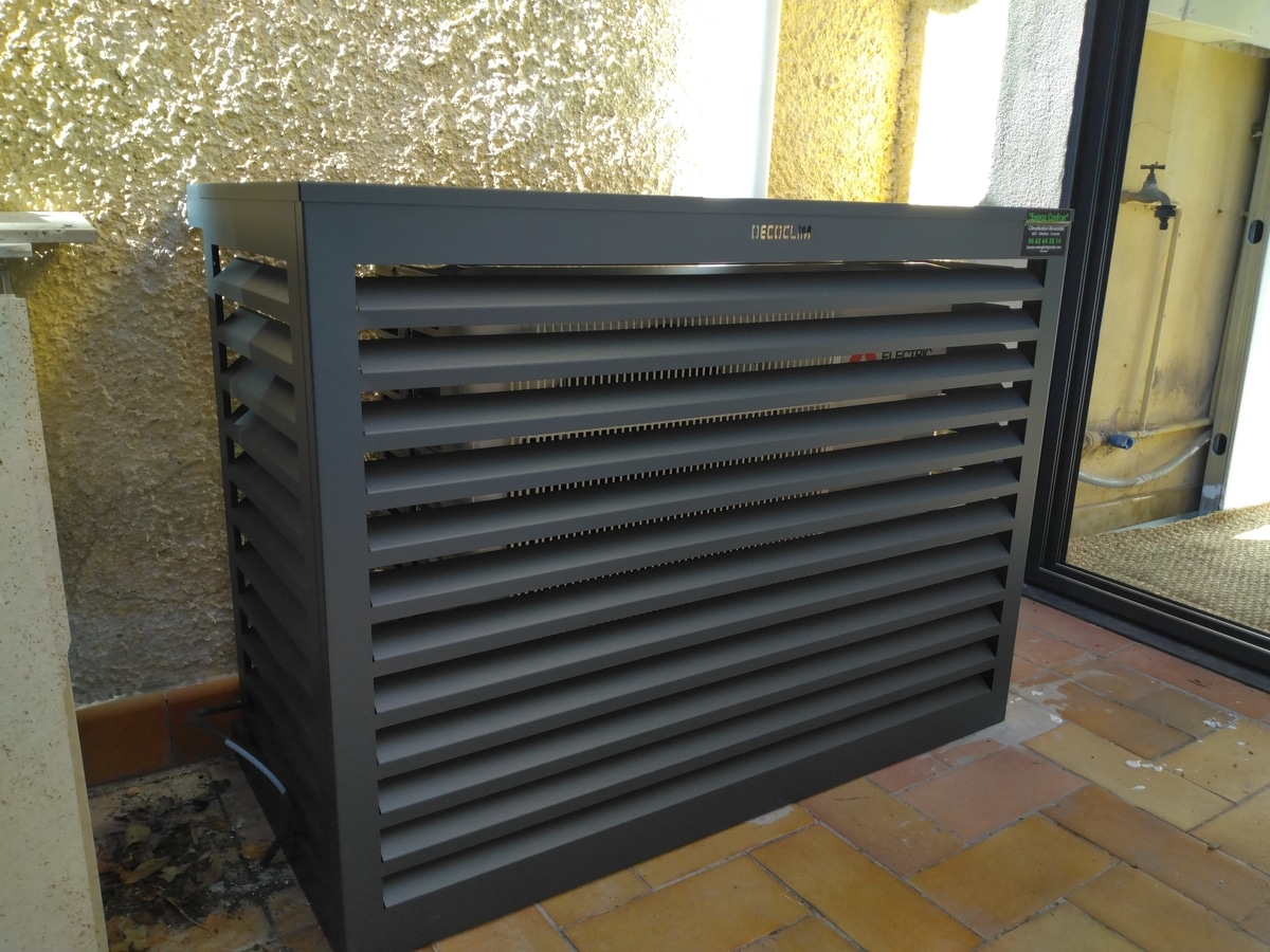 Cache-climatiseur DECOCLIM gris anthracite à lames, dissimulant une unité Mitsubishi Electric, sur patio carrelé près d'un mur texturé. Étiquette "Super Confort".